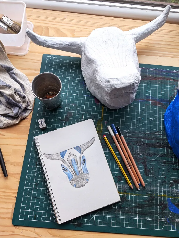 Work in progress: the unpainted papier-mâché bull on the studio worktable beside the colour sketch